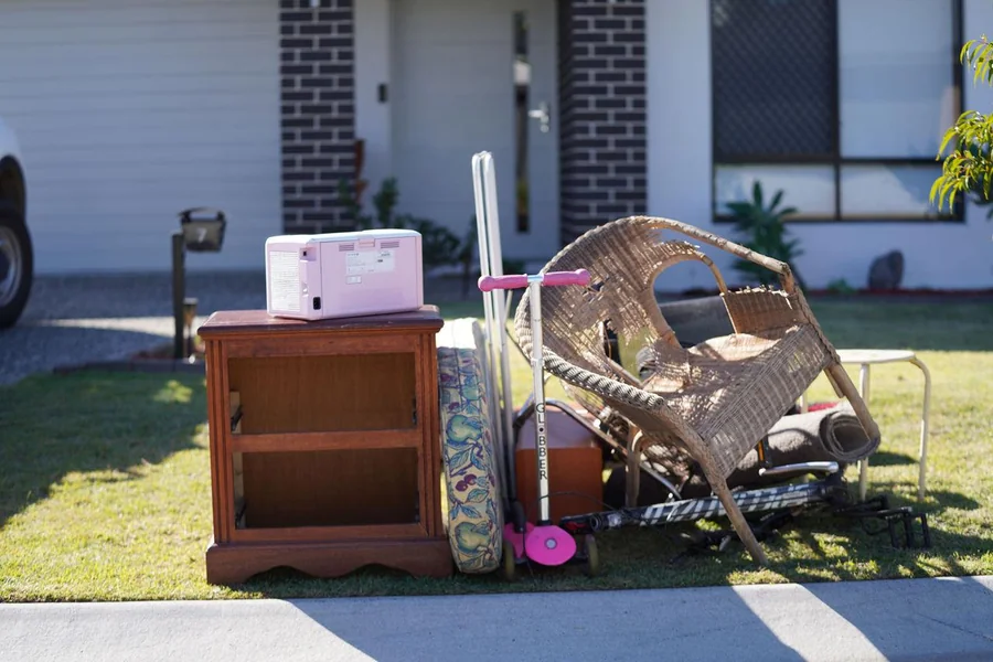 Wicker chair, cabinet and mixed household items placed on front lawn for rental property clear-out in Rivervale